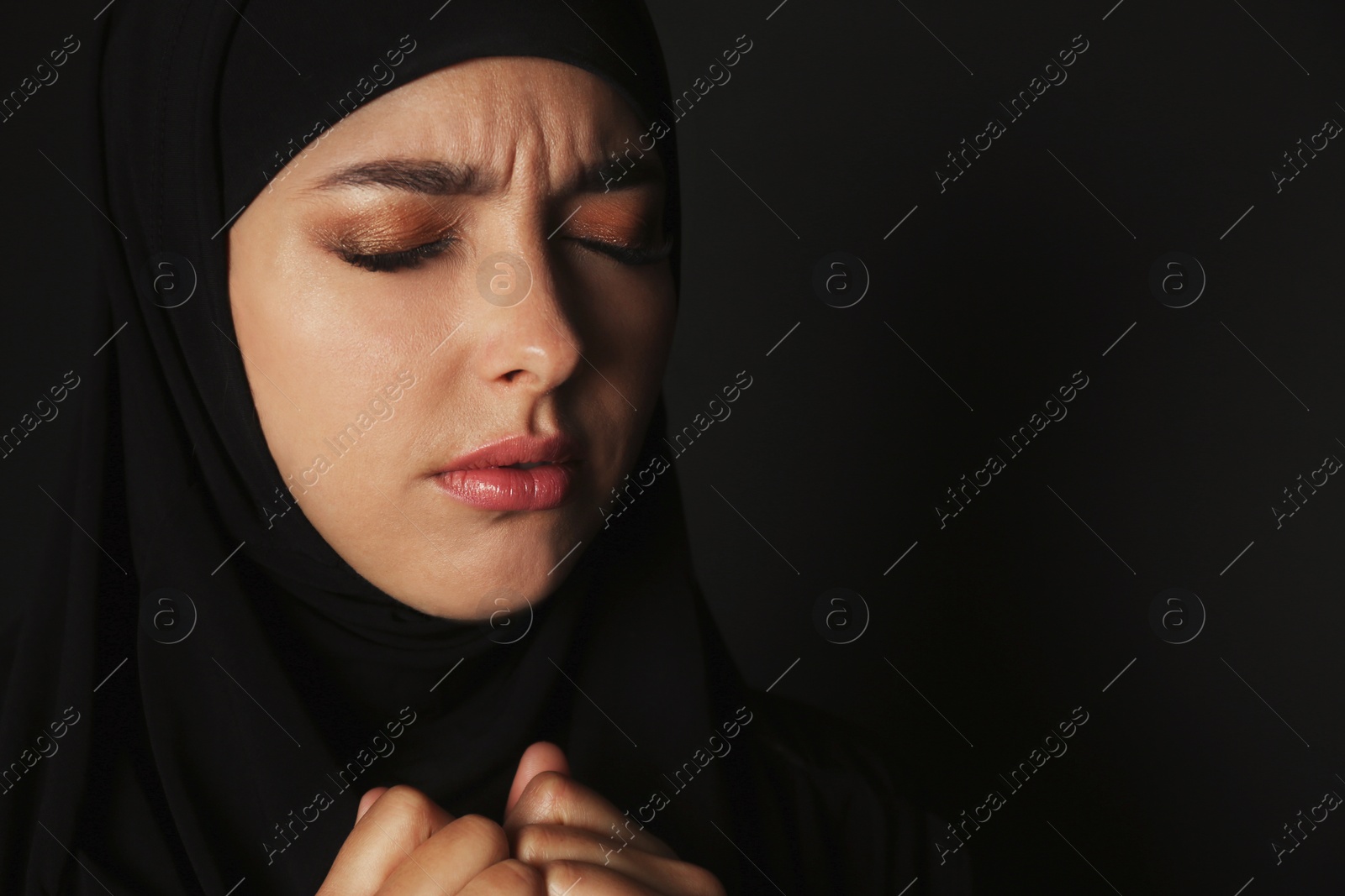 Photo of Portrait of sad Muslim woman in hijab  praying on dark background. Space for text