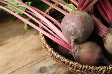 Raw ripe beets in wicker bowl on wooden table, closeup