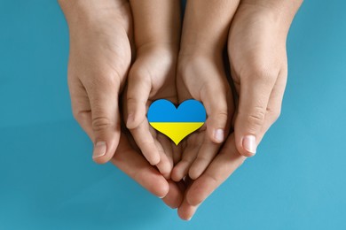 Image of Stop war in Ukraine. Mother and her child holding heart shaped symbol with colors of Ukrainian flag in hands on light blue background, closeup
