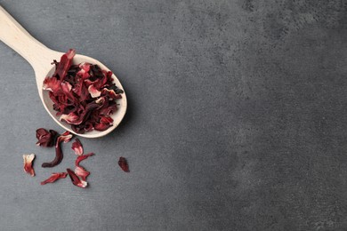 Photo of Hibiscus tea. Wooden spoon with dried roselle calyces on grey table, top view. Space for text