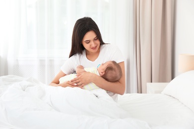 Portrait of mother with her adorable baby sitting on bed indoors