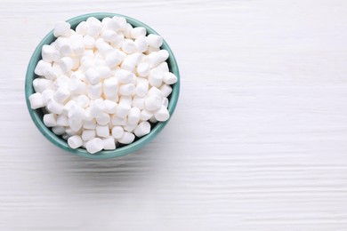 Photo of Bowl with delicious marshmallows on white wooden table, top view. Space for text