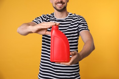 Photo of Man showing red container of motor oil on orange background, closeup