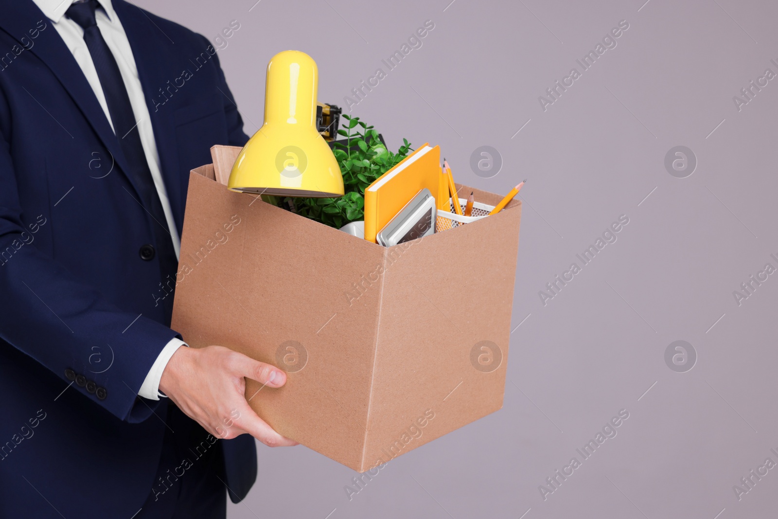 Photo of Unemployed man with box of personal office belongings on grey background, closeup. Space for text