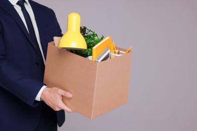 Photo of Unemployed man with box of personal office belongings on grey background, closeup. Space for text