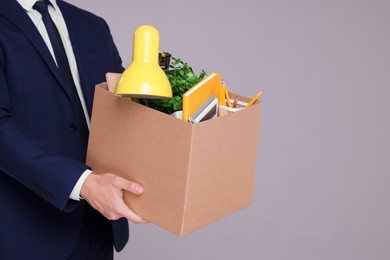 Unemployed man with box of personal office belongings on grey background, closeup. Space for text