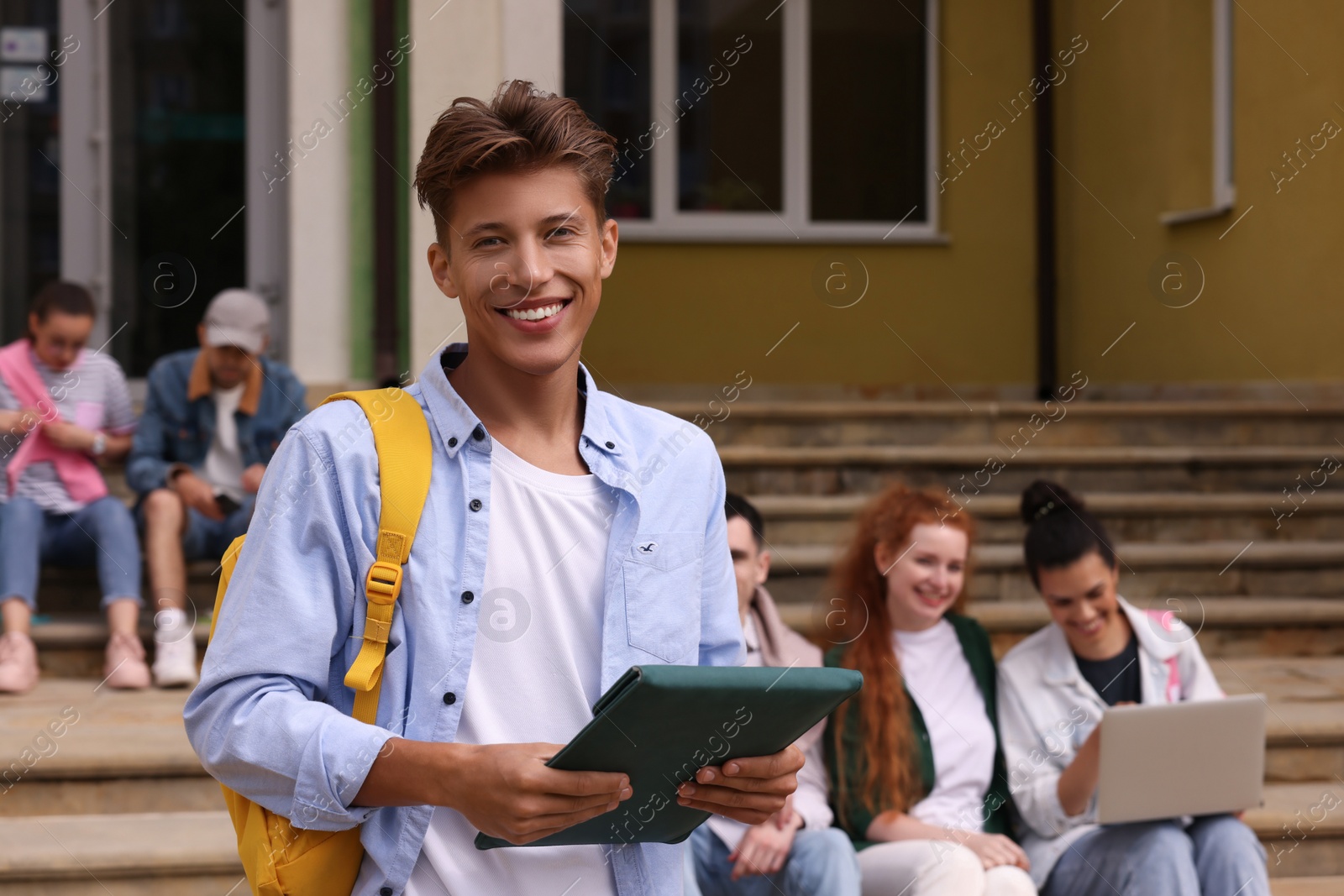 Photo of Students learning together on steps. Happy young man with tablet outdoors, selective focus