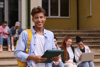 Photo of Students learning together on steps. Happy young man with tablet outdoors, selective focus