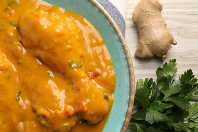 Photo of Tasty chicken curry, parsley and ginger on wooden table, flat lay