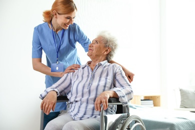 Nurse assisting elderly woman in wheelchair indoors