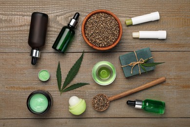 Photo of Hemp cosmetics and green leaves on wooden table, flat lay