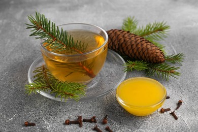 Photo of Cup with delicious immunity boosting tea, fir and ingredients on grey table, closeup
