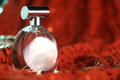 Photo of Luxury perfume in bottle on red fabric with sequins, closeup