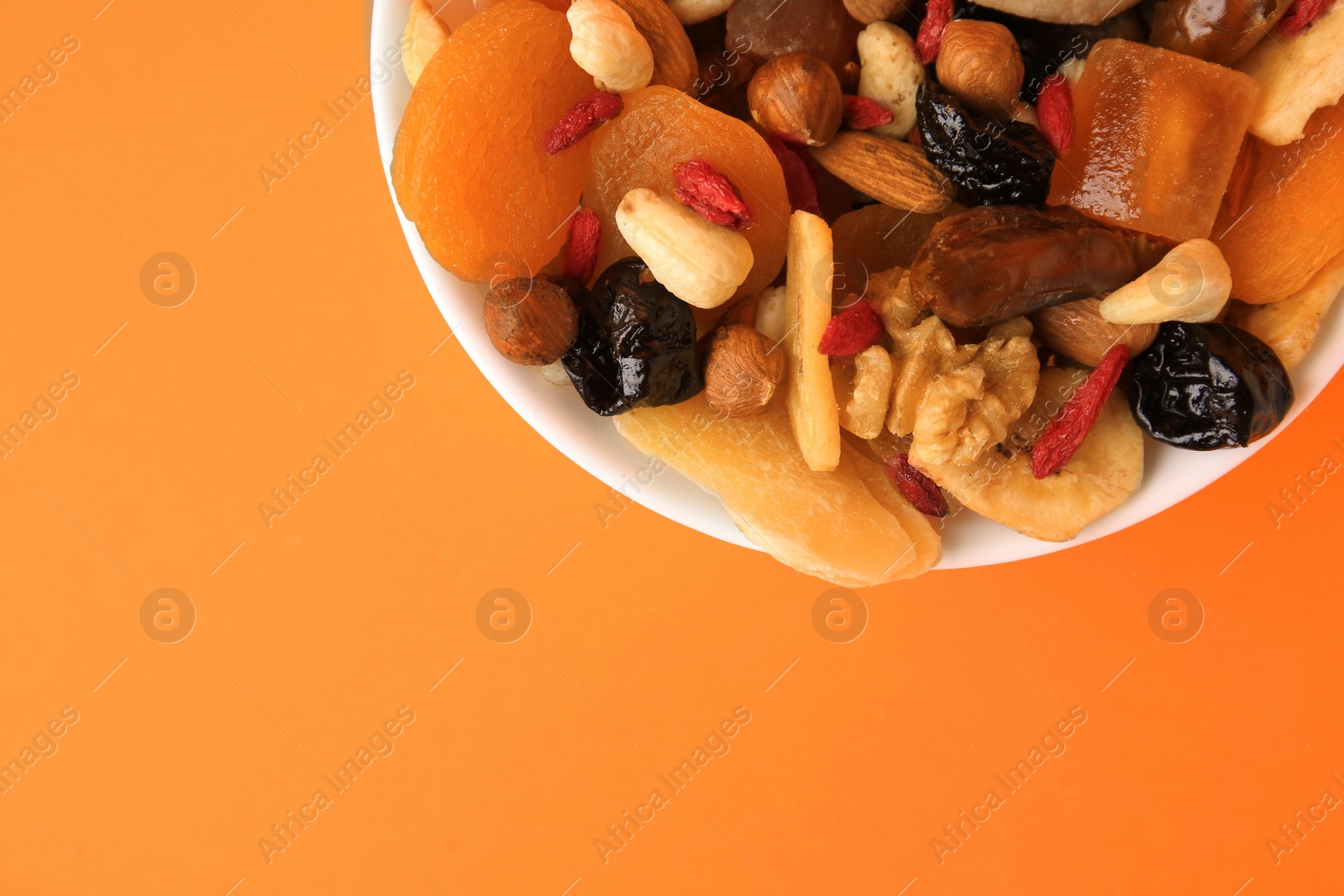 Photo of Bowl with mixed dried fruits and nuts on orange background, top view. Space for text