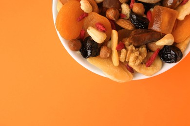 Bowl with mixed dried fruits and nuts on orange background, top view. Space for text