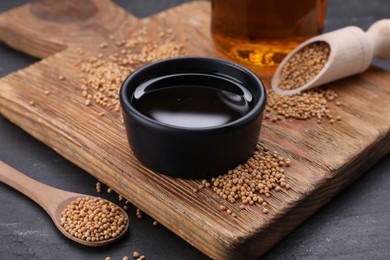 Photo of Natural oil and mustard seeds on black table, closeup