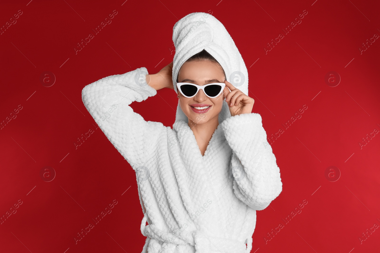 Photo of Beautiful young woman in bathrobe and sunglasses on red background