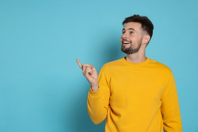 Photo of Handsome man in yellow sweatshirt pointing at something on light blue background, space for text