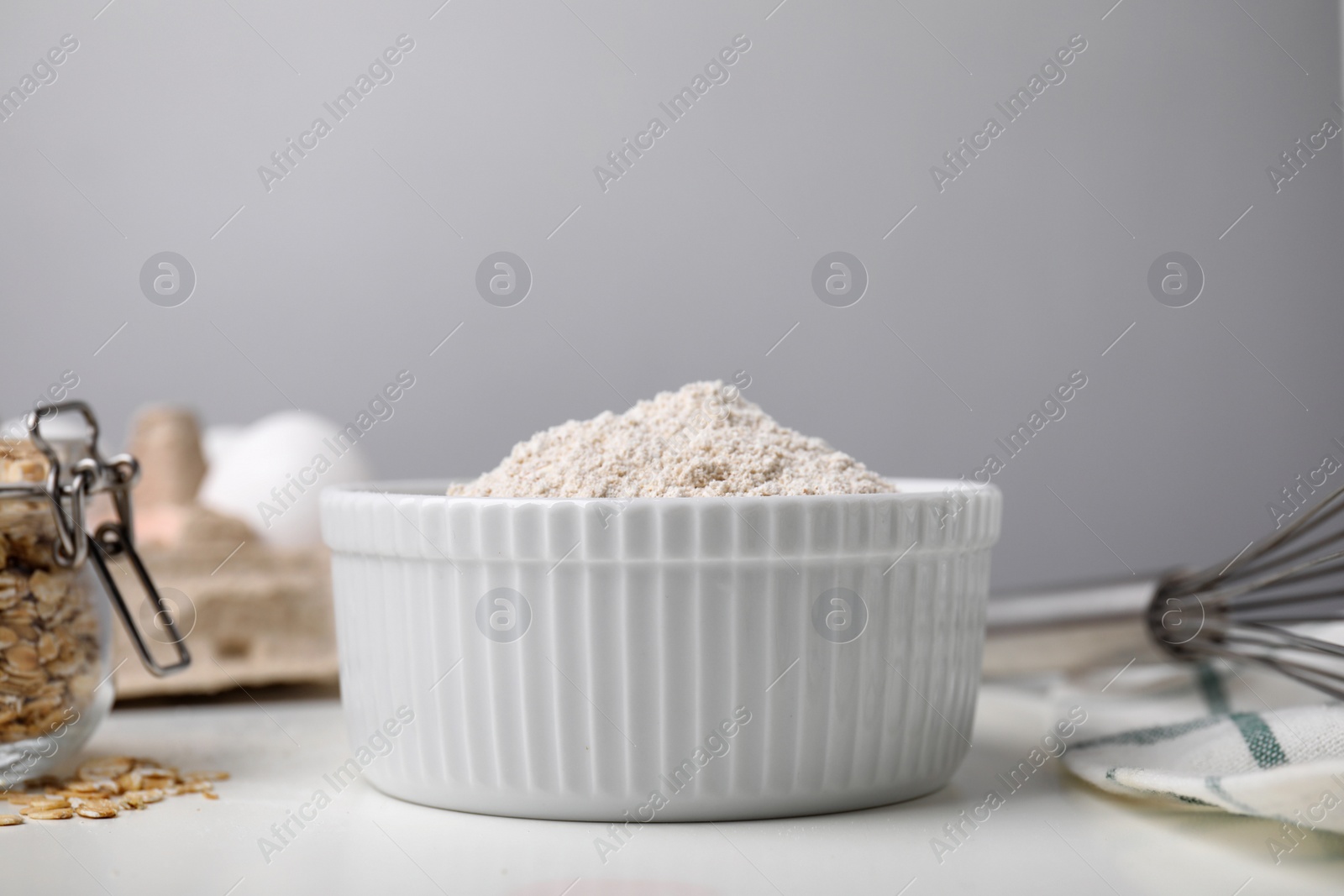 Photo of Ceramic bowl of oatmeal flour on white table, closeup