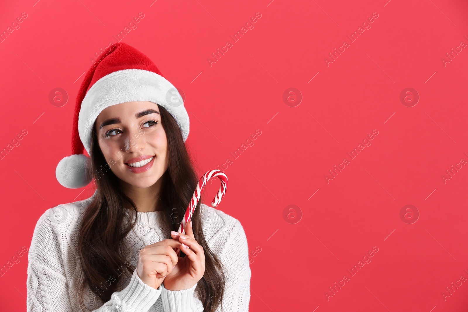 Photo of Beautiful woman in Santa Claus hat holding candy cane on red background. Space for text