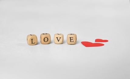 Photo of Word Love made of small wooden cubes with letters near red paper hearts on light table