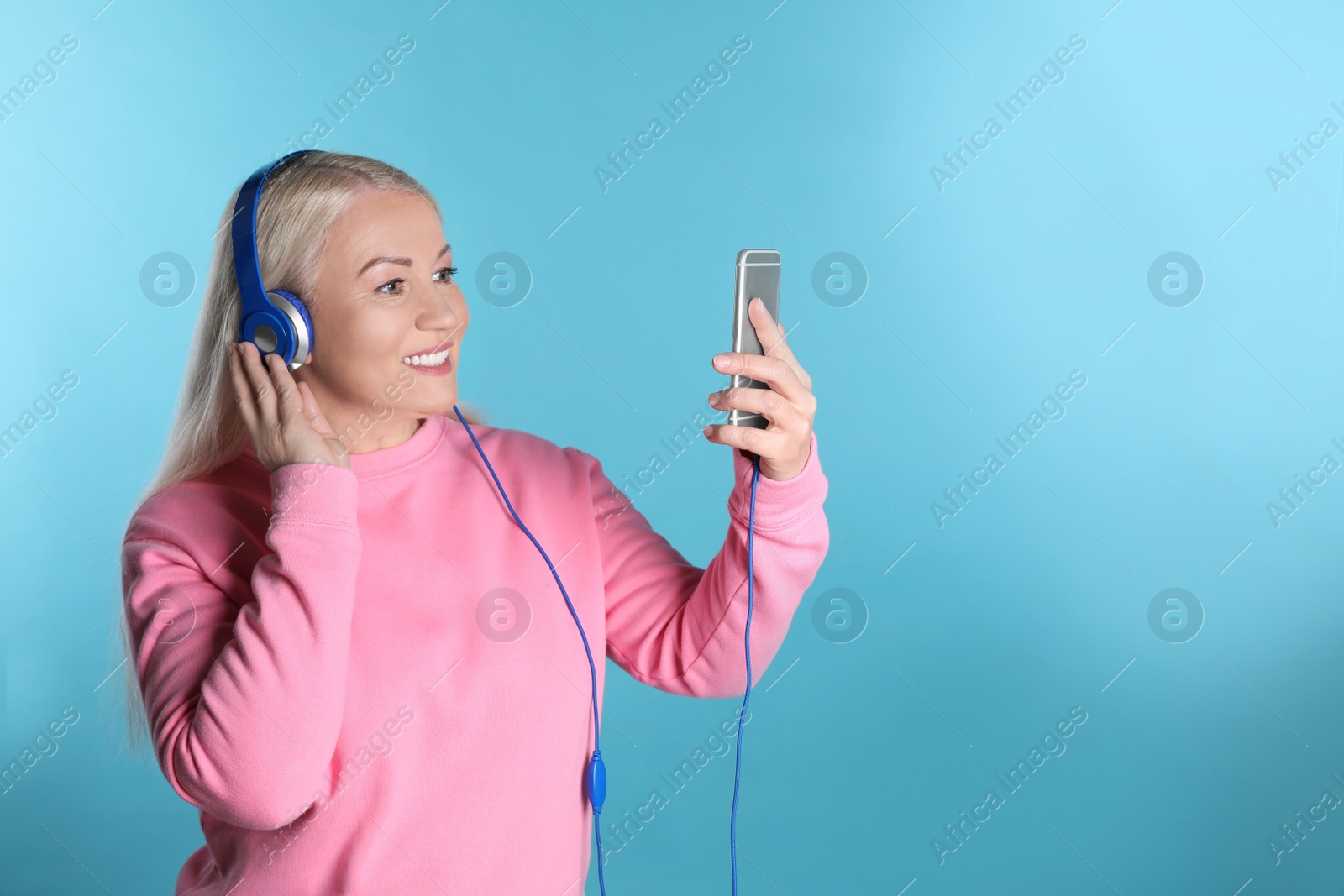 Photo of Mature woman in headphones with mobile device on color background. Space for text