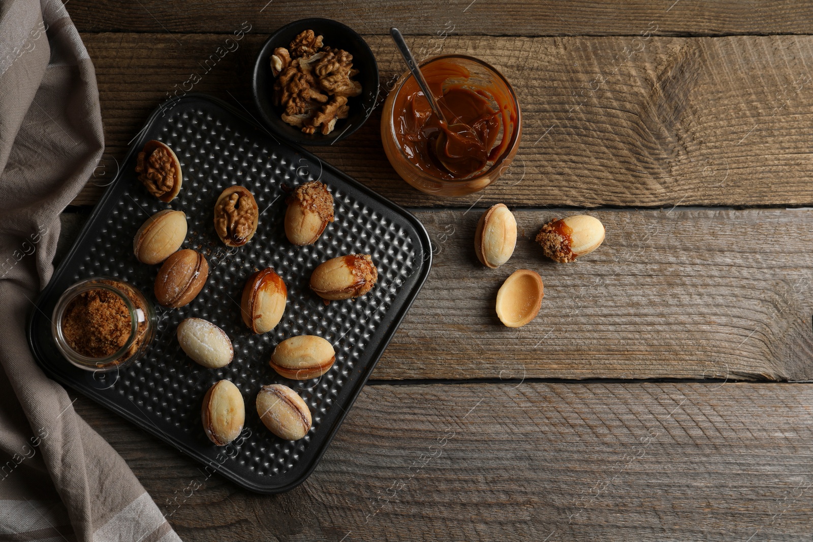 Photo of Freshly baked homemade walnut shaped cookies, boiled condensed milk and nuts on wooden table, flat lay. Space for text