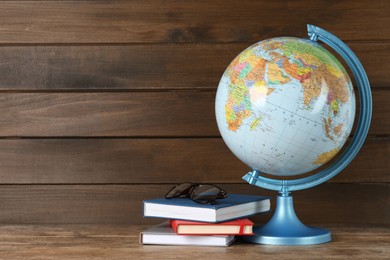 Globe, books and eyeglasses on wooden table, space for text. Geography lesson