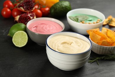 Photo of Different kinds of tasty hummus, nachos and ingredients on black table