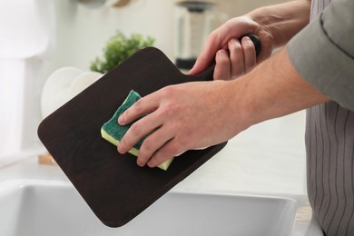Photo of Man washing dark wooden cutting board at sink in kitchen, closeup