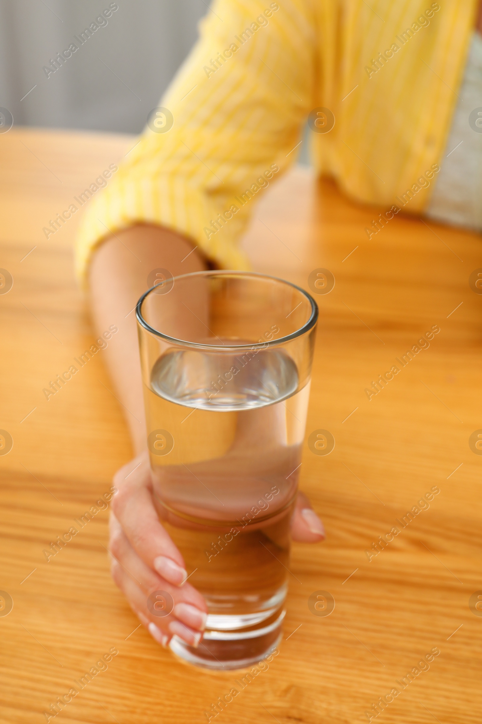 Photo of Woman holding glass of water at wooden table, closeup. Refreshing drink