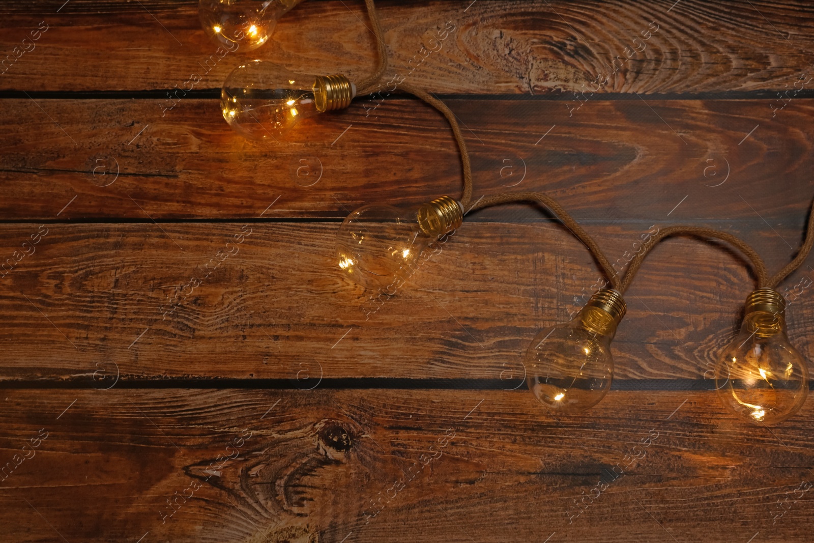 Photo of String lights with lamp bulbs on wooden table, top view. Space for text