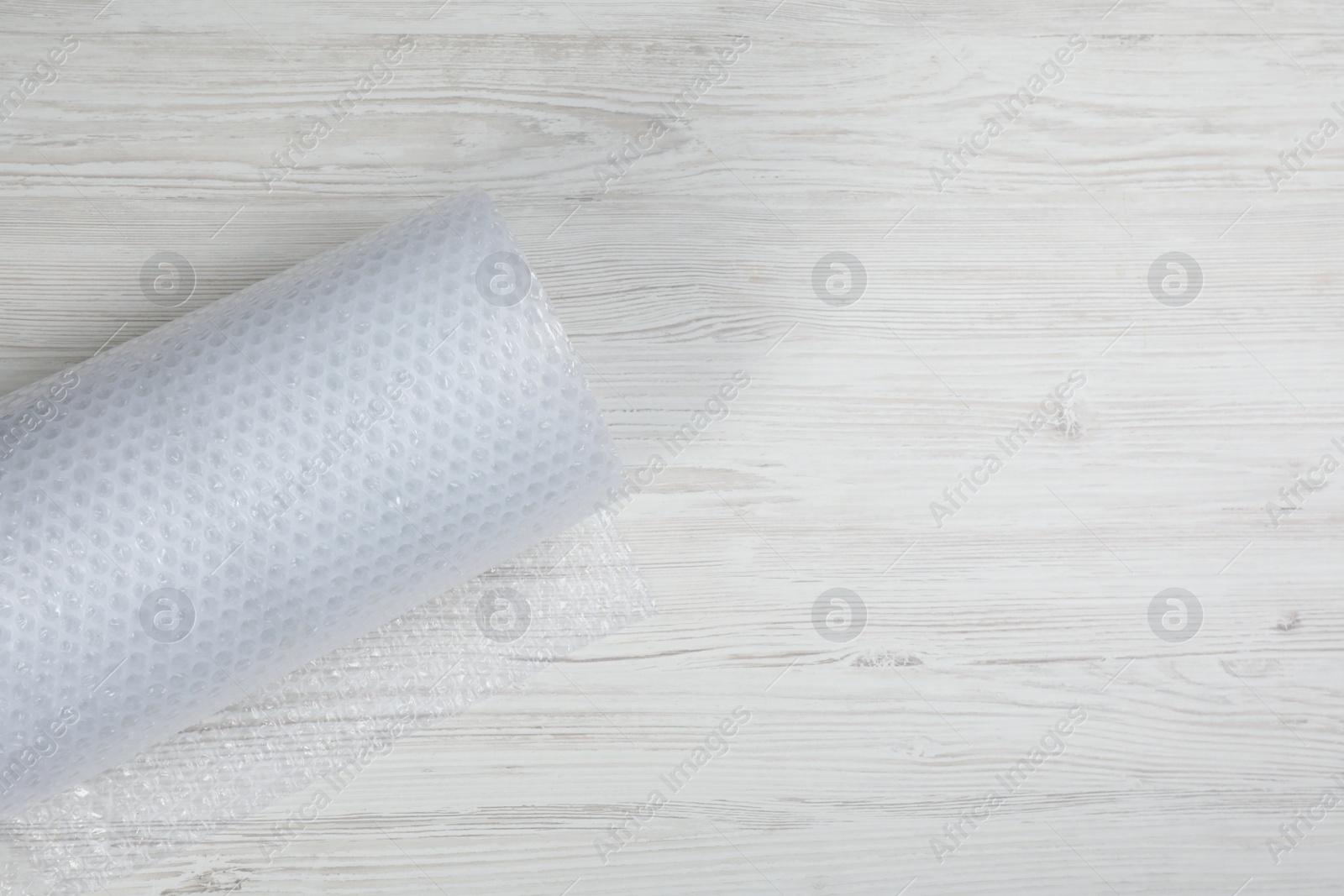 Photo of Bubble wrap roll on white wooden background, top view. Space for text