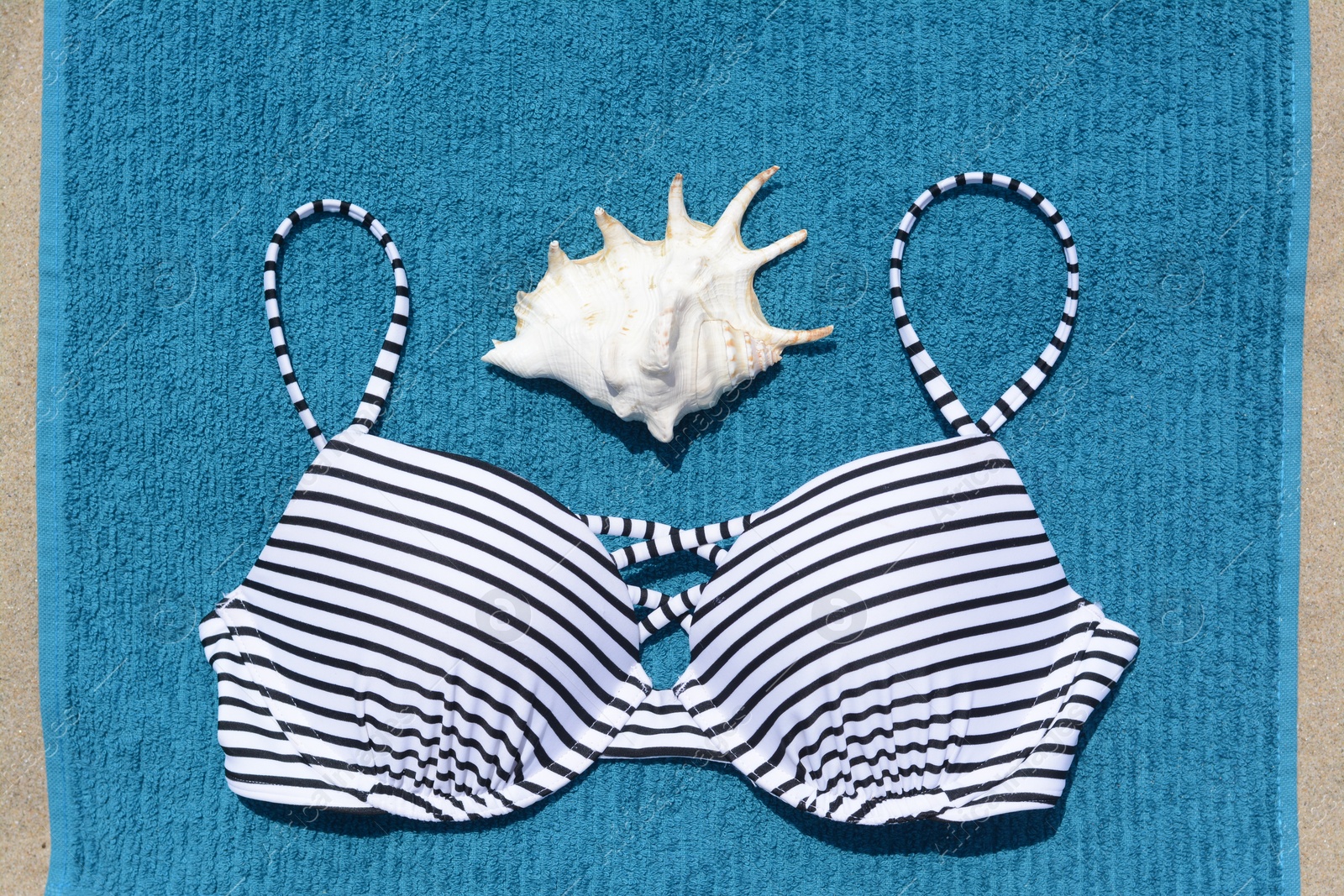 Photo of Blue beach towel, seashell and swimsuit on sand, top view