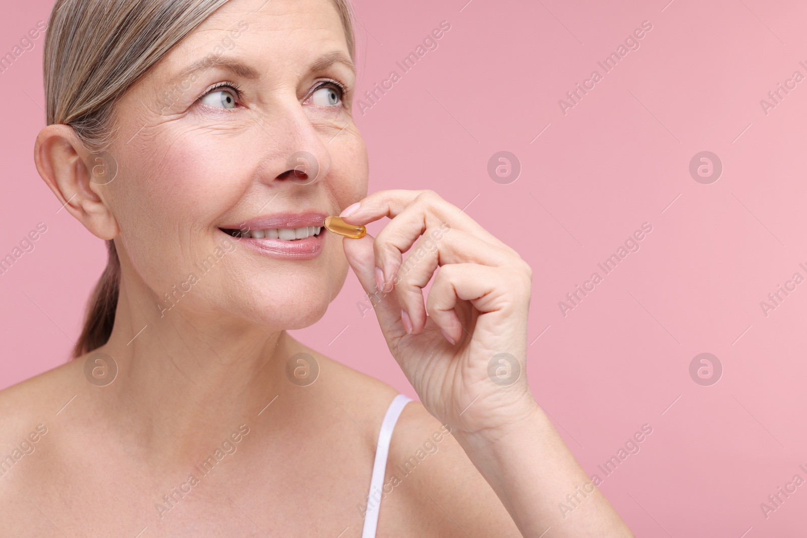 Photo of Beautiful woman taking vitamin capsule on pink background, space for text