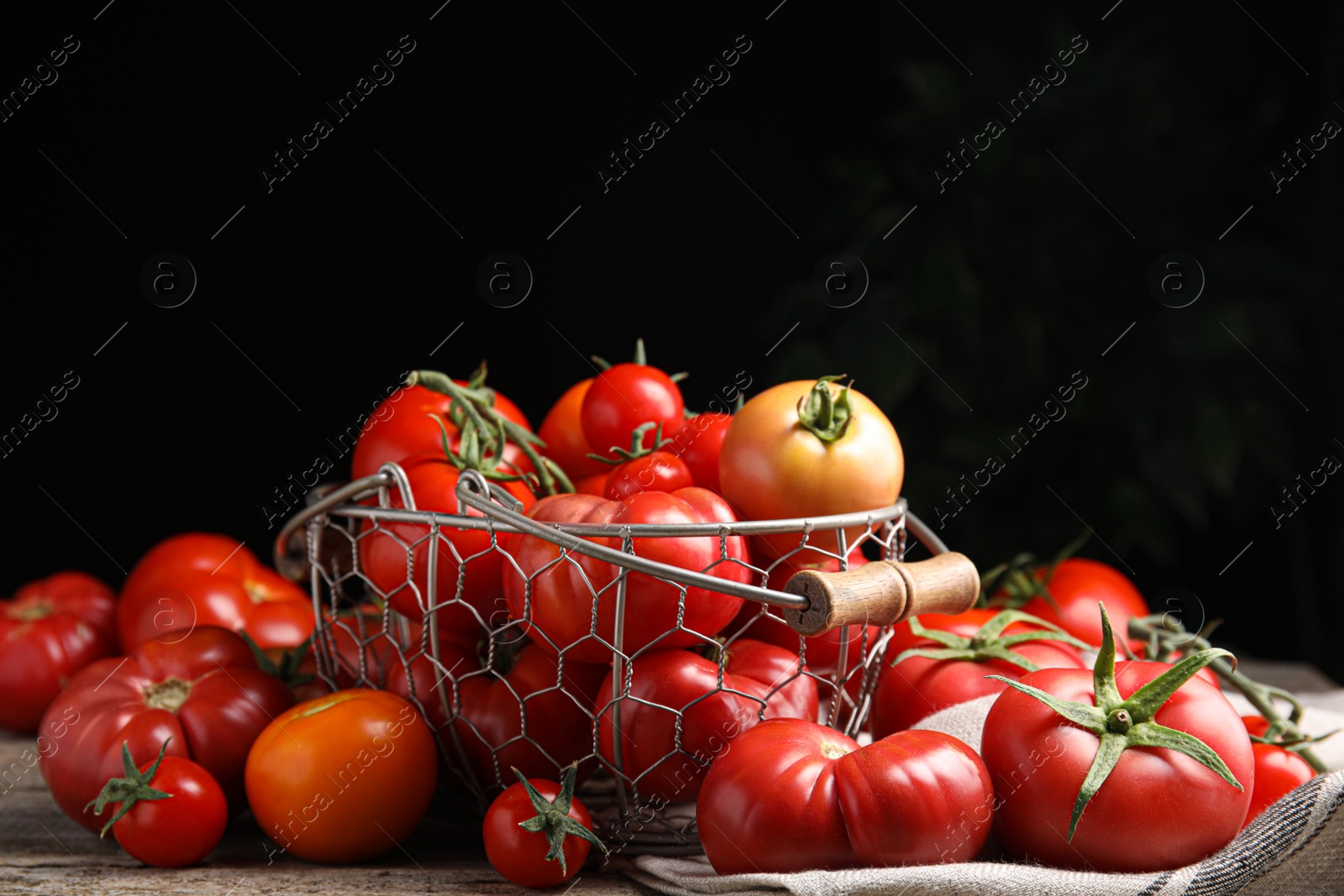 Photo of Many different ripe tomatoes on wooden table against dark background