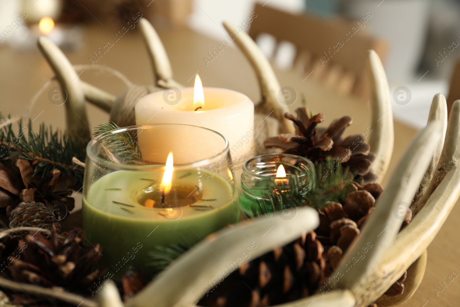 Photo of Burning scented conifer candles with Christmas decor on table, closeup