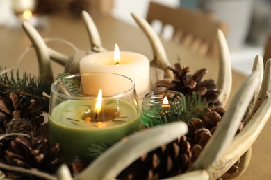Photo of Burning scented conifer candles with Christmas decor on table, closeup