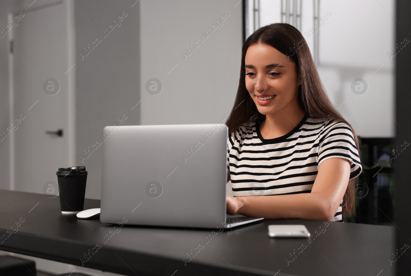 Photo of Happy young woman using laptop at table in hostel