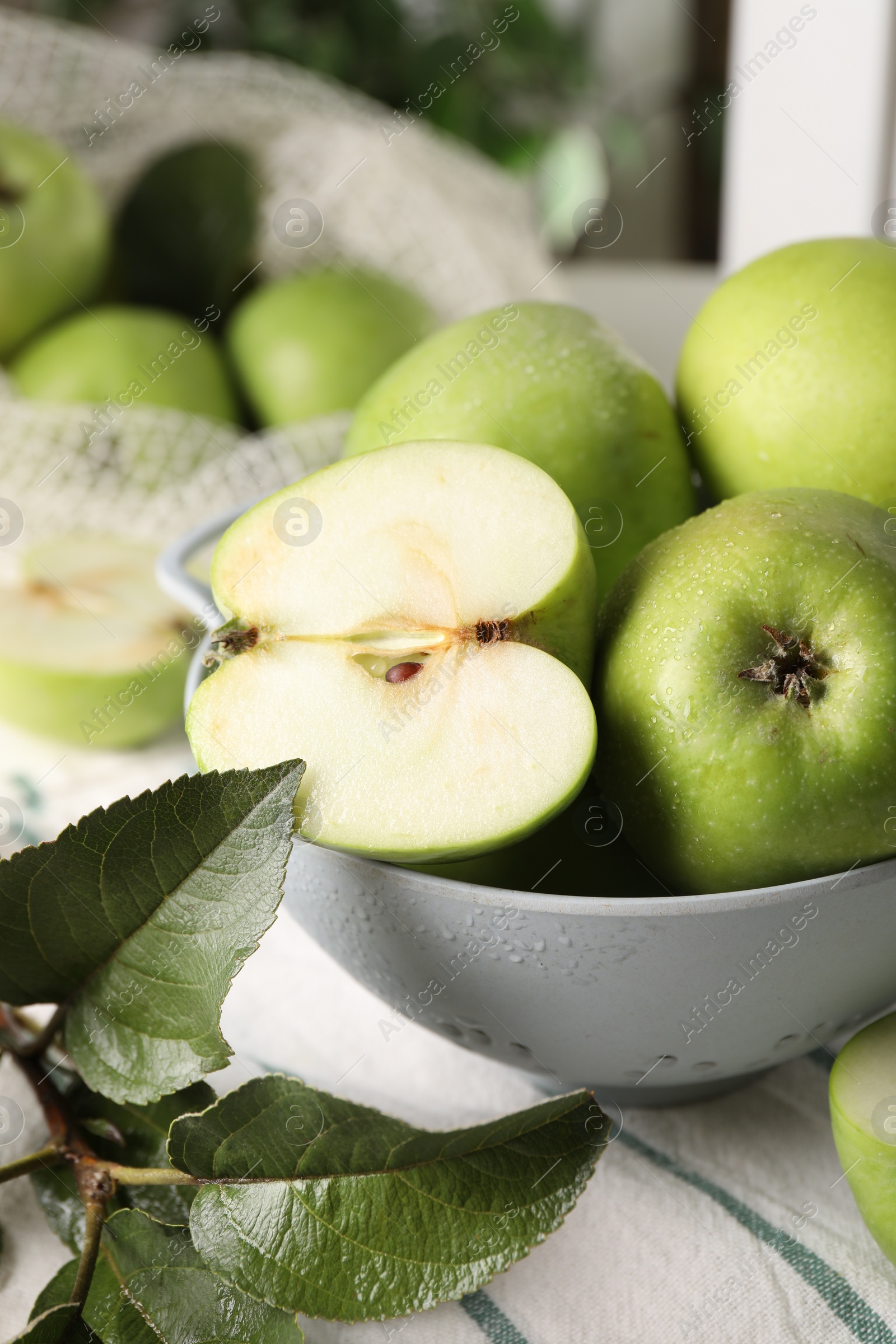 Photo of Fresh green apples with water drops and leaves on white striped tablecloth, closeup