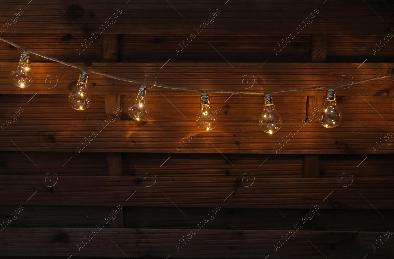 Photo of Garland of lamp bulbs hanging on wooden wall. String lights