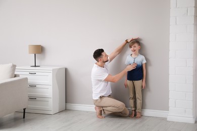 Photo of Father measuring height of his son near wall at home