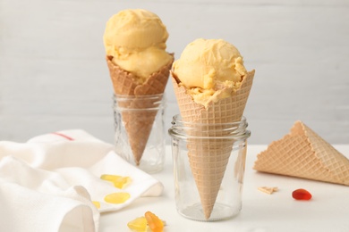 Delicious yellow ice cream in wafer cones and jelly candies on white table