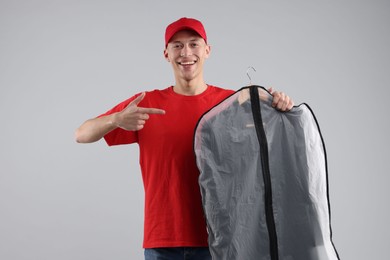 Dry-cleaning delivery. Happy courier holding garment cover with clothes on light grey background