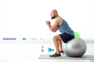 Overweight man doing exercise with fitness ball in gym