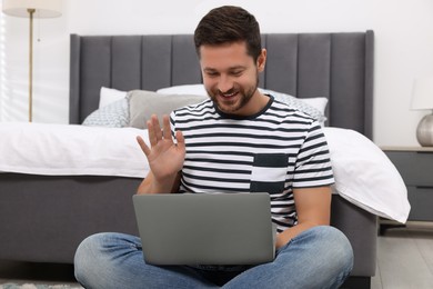 Happy man greeting someone during video chat via laptop in bedroom