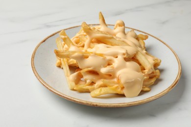 Photo of Delicious French fries with cheese sauce on white marble table, closeup