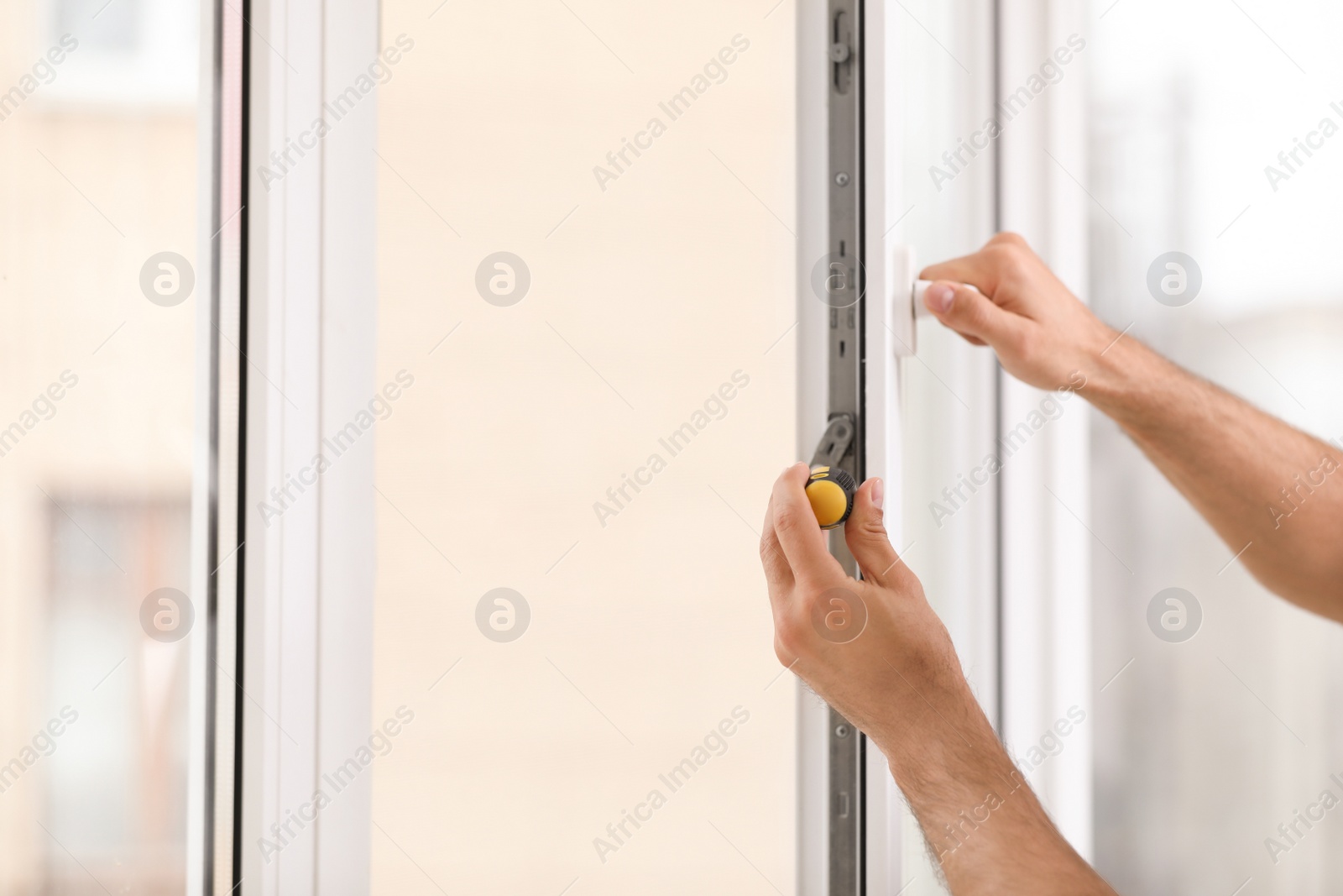 Photo of Construction worker repairing plastic window with screwdriver indoors, closeup