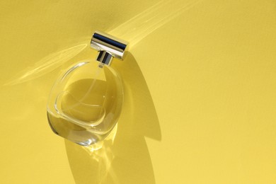 Photo of Luxury women's perfume. Sunlit glass bottle on yellow background, top view. Space for text
