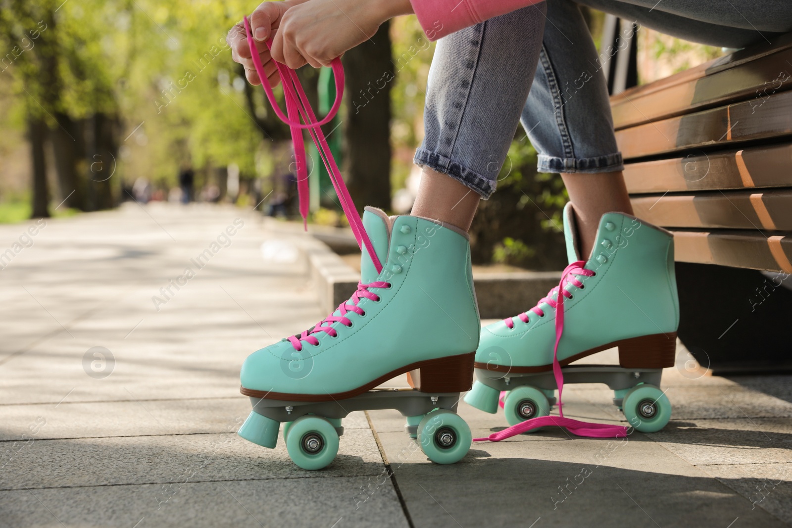 Photo of Woman lacing roller skates while sitting on bench outdoors, closeup